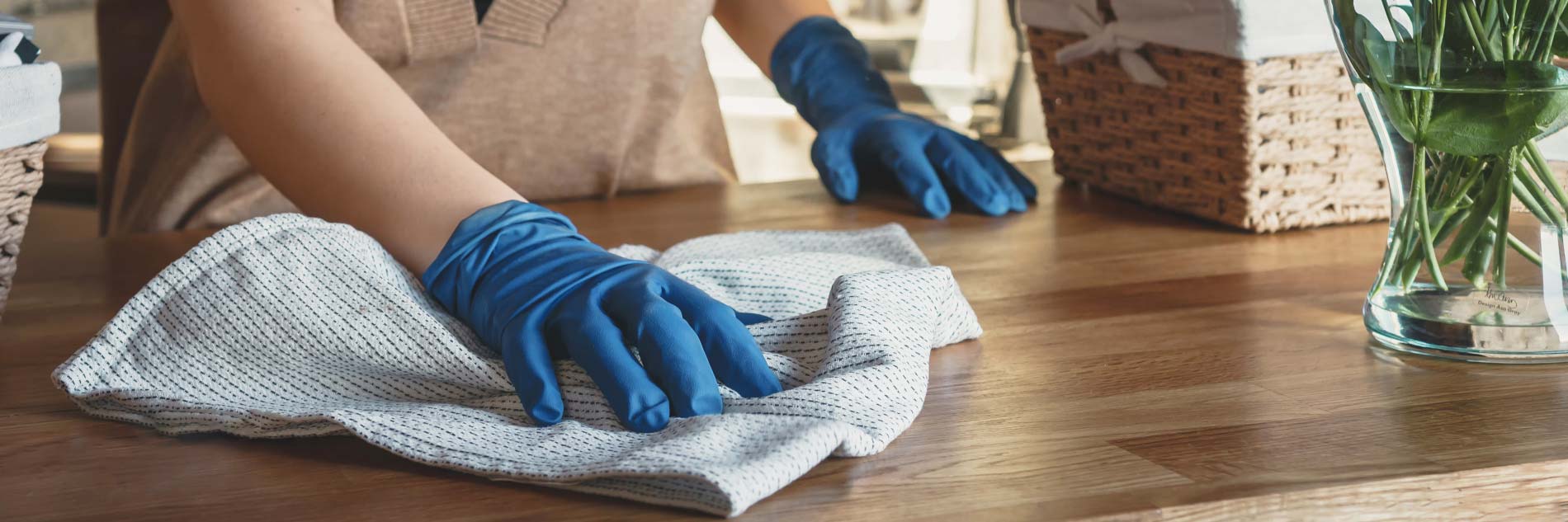 Photographie d'une main portant des gants de ménage et faisant la poussière sur un meuble en bois