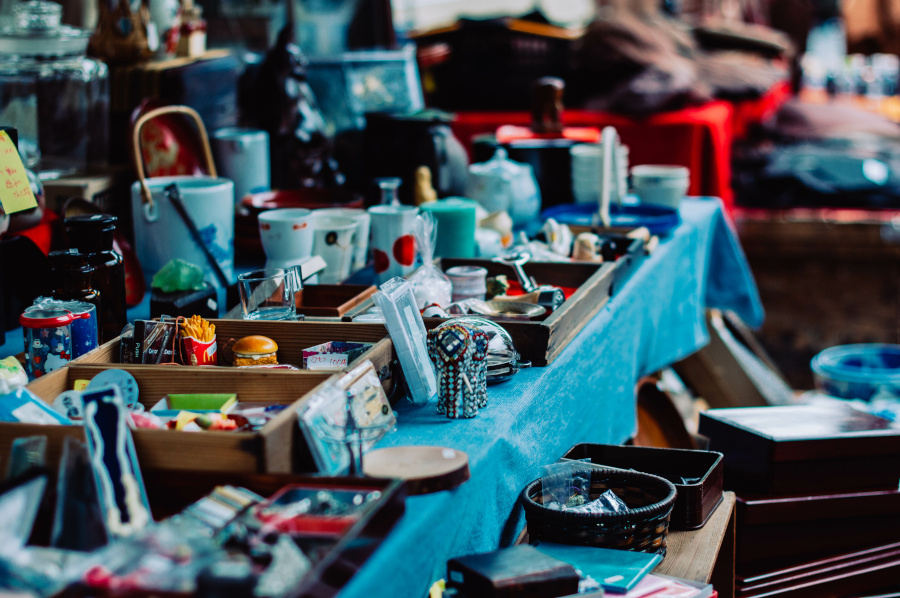 Photographie de bijoux, montres et bibelots sur un stand de vide grenier dans une teinte bleutée.